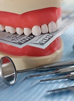 A denture holding hundred-dollar bills next to dental instruments