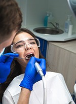 Woman with brown hair undergoing root canal performed by dentist with blue gloves