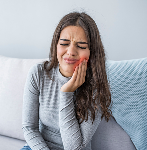 Woman holding her cheek in pain before seeing an emergency dentist in Norwood