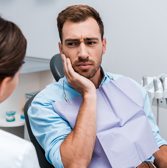 Man holding his cheek in pain while talking to his emergency dentist