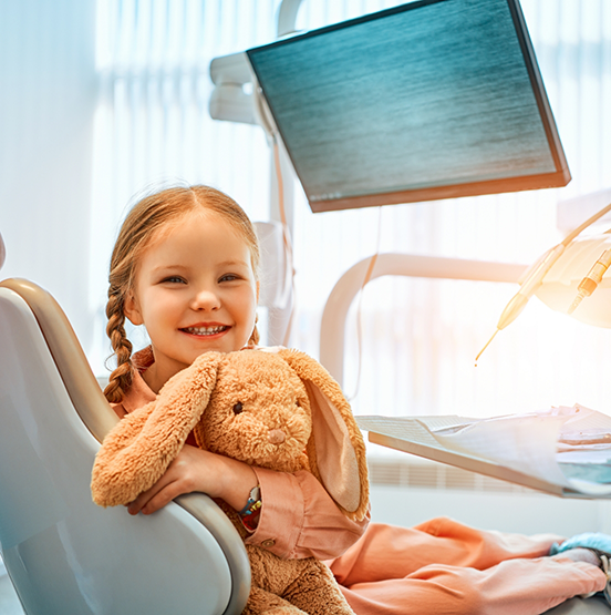 Smiling girl in a dental chair holding a stuffed rabbit