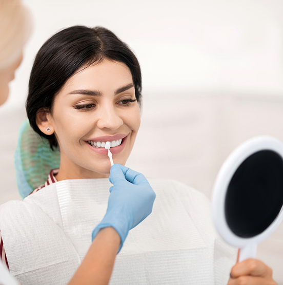 Woman smiling while a dentist holds a veneer in front of her teeth